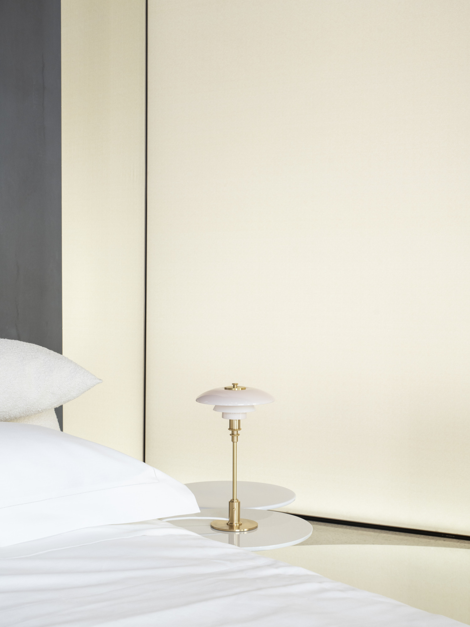 PH 2/1 table lamp on a bedside table with a soft yellow backdrop, © 2025 Louis Poulsen.